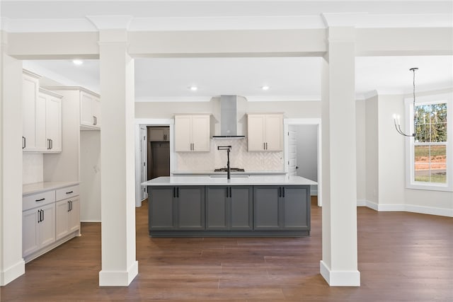 kitchen featuring a center island with sink, wall chimney range hood, backsplash, and dark hardwood / wood-style flooring