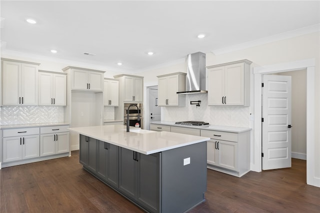 kitchen with wall chimney range hood, dark hardwood / wood-style floors, a kitchen island with sink, and backsplash