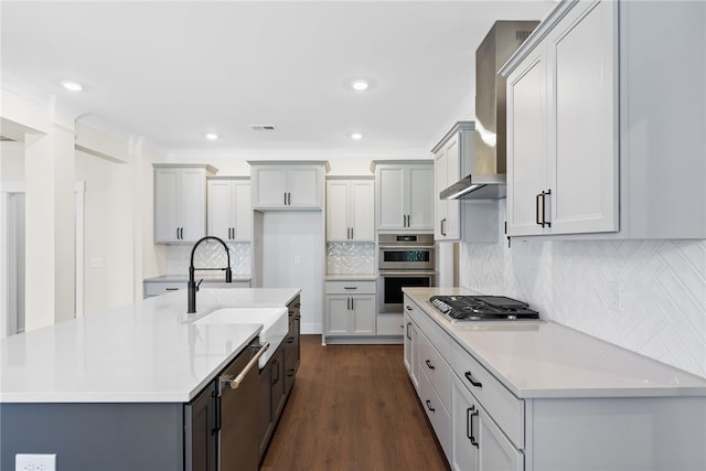 kitchen featuring tasteful backsplash, wall chimney range hood, appliances with stainless steel finishes, an island with sink, and dark hardwood / wood-style flooring