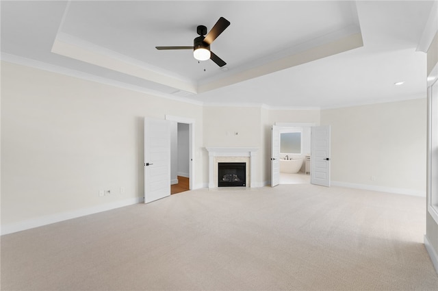 unfurnished living room featuring ceiling fan, a raised ceiling, crown molding, and light colored carpet