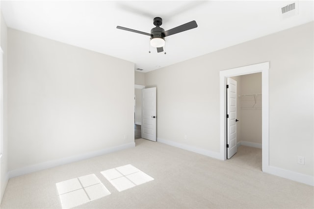 unfurnished bedroom featuring a spacious closet, ceiling fan, a closet, and light colored carpet