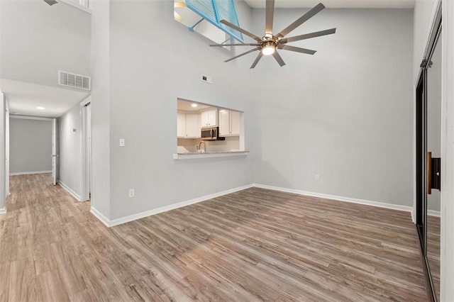 unfurnished living room featuring light wood-type flooring, a ceiling fan, a towering ceiling, and visible vents