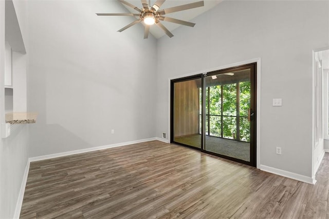 unfurnished room with baseboards, wood finished floors, and high vaulted ceiling