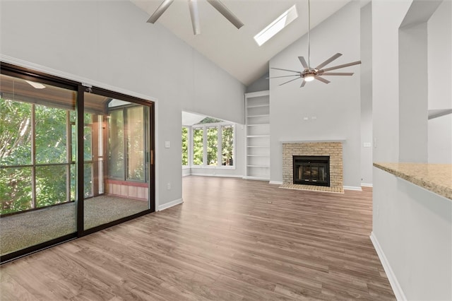 unfurnished living room featuring wood-type flooring, a fireplace, high vaulted ceiling, a skylight, and ceiling fan