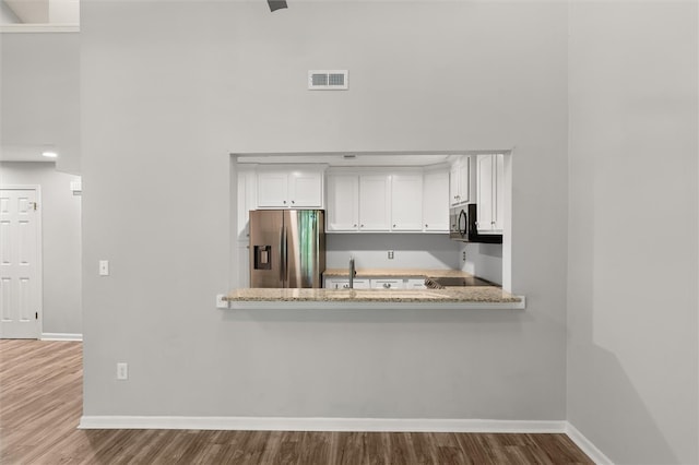 kitchen featuring white cabinets, appliances with stainless steel finishes, hardwood / wood-style floors, and light stone countertops