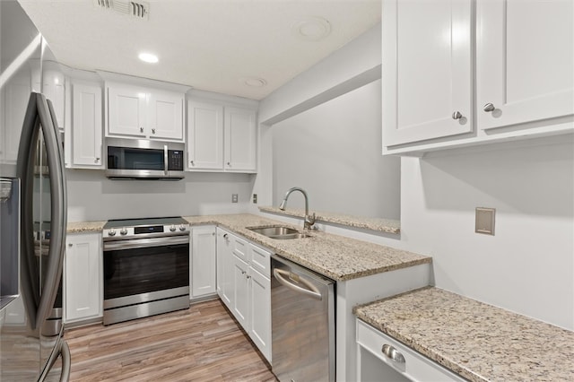 kitchen with light wood-type flooring, sink, white cabinetry, appliances with stainless steel finishes, and light stone countertops