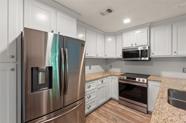 kitchen with light stone countertops, appliances with stainless steel finishes, light wood-type flooring, and white cabinetry