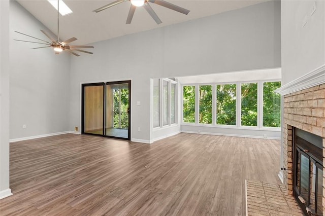unfurnished living room with a brick fireplace, ceiling fan, wood finished floors, and high vaulted ceiling