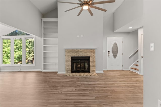 unfurnished living room with a brick fireplace, light wood-type flooring, ceiling fan, and high vaulted ceiling