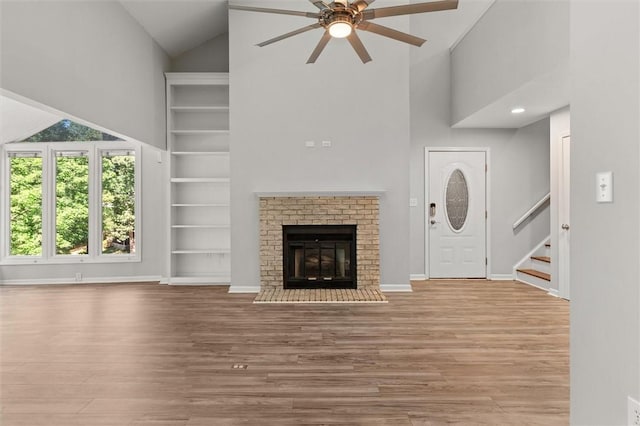 unfurnished living room with high vaulted ceiling, ceiling fan, stairs, and wood finished floors