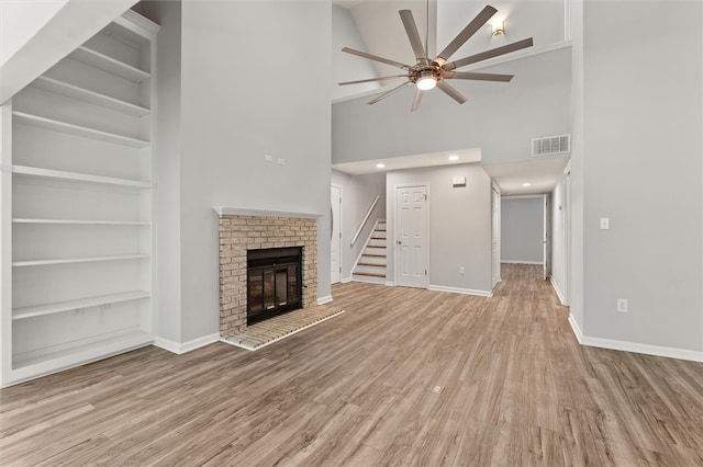 unfurnished living room with ceiling fan, built in features, high vaulted ceiling, a fireplace, and light wood-type flooring