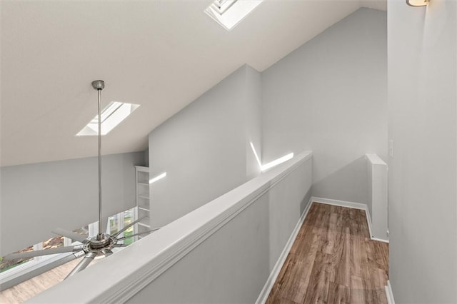 corridor featuring baseboards, an upstairs landing, wood finished floors, and lofted ceiling with skylight