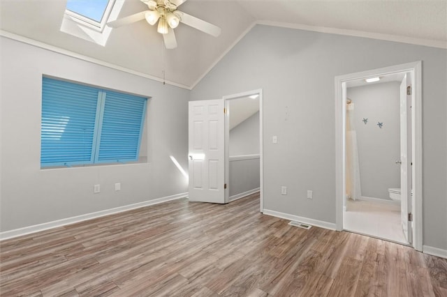 unfurnished bedroom featuring visible vents, wood finished floors, vaulted ceiling with skylight, and ensuite bath