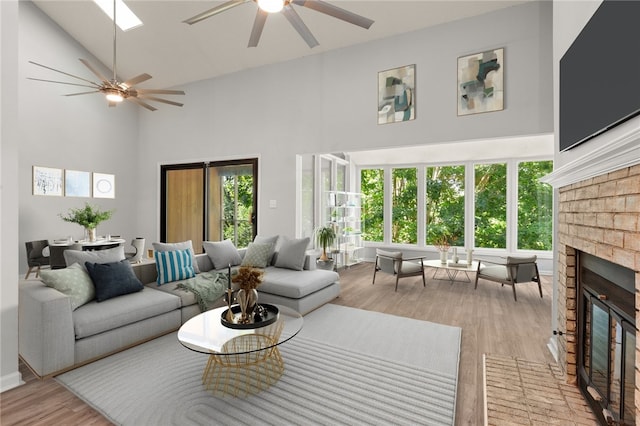 living room featuring a ceiling fan, high vaulted ceiling, light wood-style flooring, and a fireplace