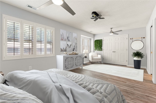 bedroom featuring visible vents, a textured ceiling, wood finished floors, and multiple windows