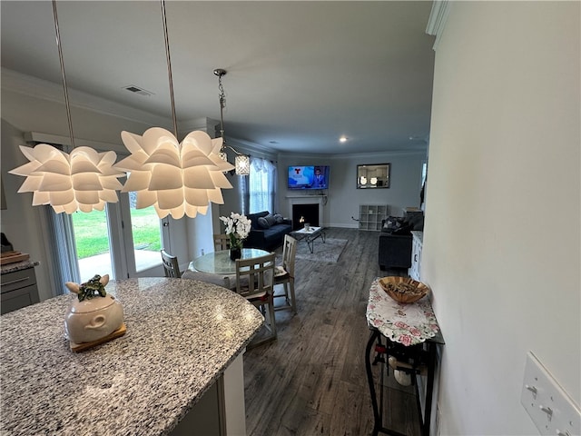 kitchen with light stone countertops, hanging light fixtures, ornamental molding, and dark hardwood / wood-style flooring