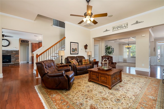 living room with ceiling fan with notable chandelier, a stone fireplace, ornamental molding, and hardwood / wood-style floors