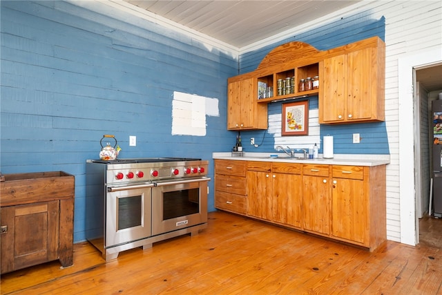 kitchen featuring light wood-type flooring, sink, wood walls, designer stove, and crown molding