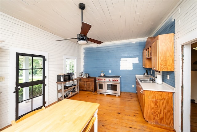 kitchen featuring hanging light fixtures, sink, wooden walls, light hardwood / wood-style flooring, and range with two ovens