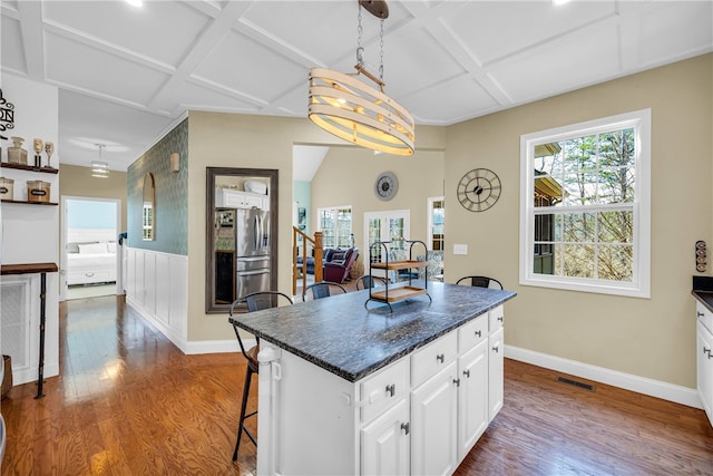 kitchen with a kitchen island, wood-type flooring, white cabinetry, coffered ceiling, and a breakfast bar