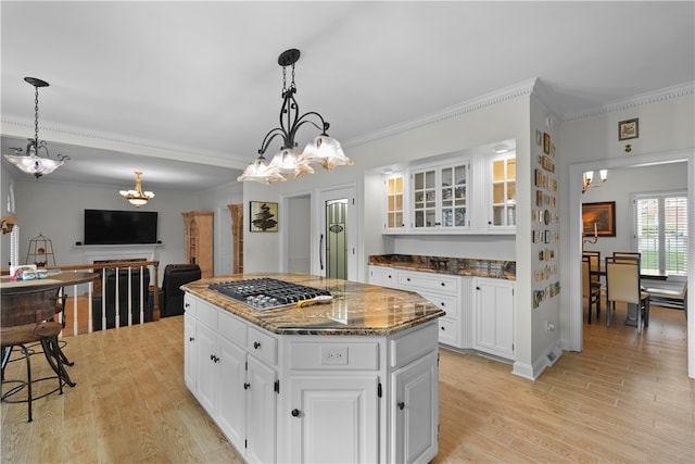 kitchen with ornamental molding, dark stone counters, white cabinets, a center island, and light hardwood / wood-style floors