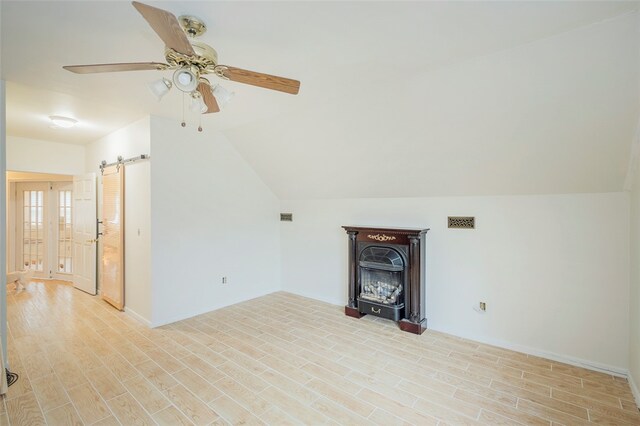 additional living space with a barn door, ceiling fan, vaulted ceiling, and light wood-type flooring