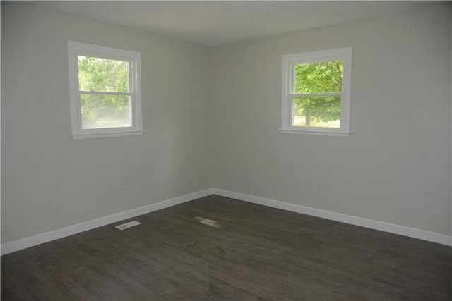 unfurnished room with plenty of natural light, baseboards, visible vents, and dark wood-style flooring