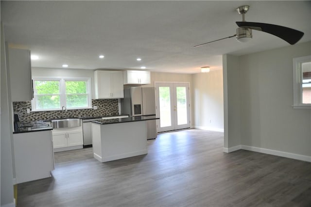 kitchen featuring stainless steel appliances, a center island, backsplash, dark countertops, and wood finished floors