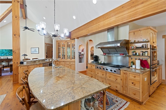 kitchen with hanging light fixtures, wall chimney exhaust hood, light hardwood / wood-style flooring, appliances with stainless steel finishes, and vaulted ceiling