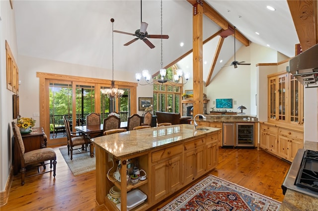 kitchen with wine cooler, beamed ceiling, an island with sink, high vaulted ceiling, and light wood-type flooring