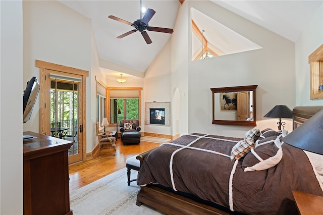 bedroom featuring light hardwood / wood-style floors, access to outside, high vaulted ceiling, a multi sided fireplace, and ceiling fan