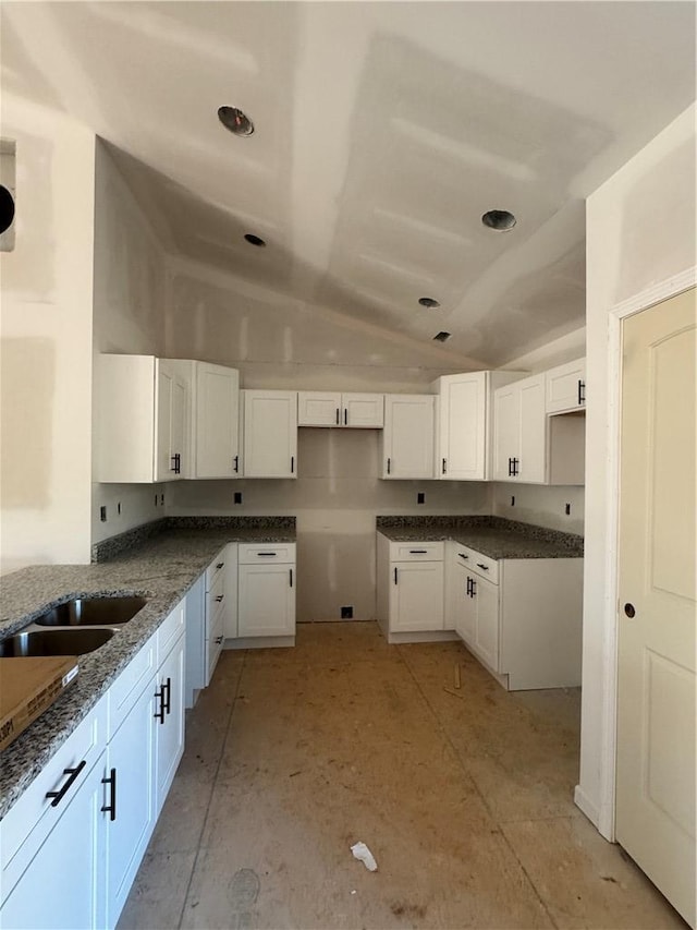 kitchen featuring vaulted ceiling, dark stone countertops, and white cabinets