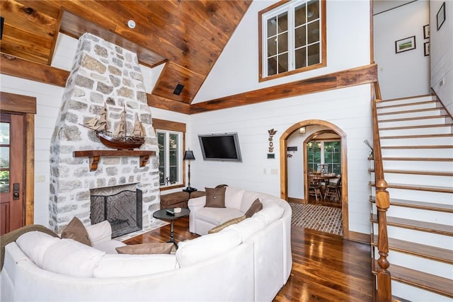 living room featuring wood ceiling, high vaulted ceiling, wood walls, and a stone fireplace