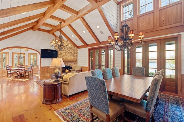 dining area featuring wood-type flooring, wood walls, a stone fireplace, and an inviting chandelier