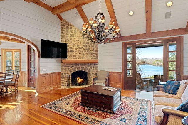 living room featuring a stone fireplace, wooden walls, light hardwood / wood-style floors, high vaulted ceiling, and beam ceiling