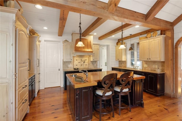 kitchen featuring dark wood-type flooring, beamed ceiling, tasteful backsplash, and an island with sink