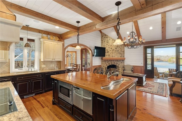 kitchen featuring wooden counters, beamed ceiling, an island with sink, light wood-type flooring, and stainless steel microwave