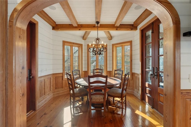 dining room featuring light hardwood / wood-style floors, a chandelier, beam ceiling, and french doors