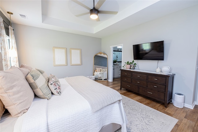 bedroom with a raised ceiling, dark hardwood / wood-style floors, and ceiling fan