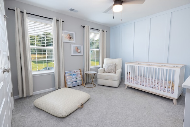 carpeted bedroom with ceiling fan, a nursery area, and multiple windows