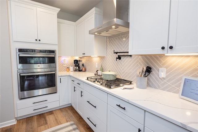 kitchen with white cabinets, backsplash, stainless steel appliances, hardwood / wood-style floors, and wall chimney range hood