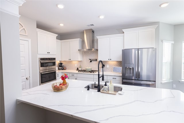 kitchen featuring light stone counters, sink, white cabinetry, wall chimney range hood, and stainless steel appliances