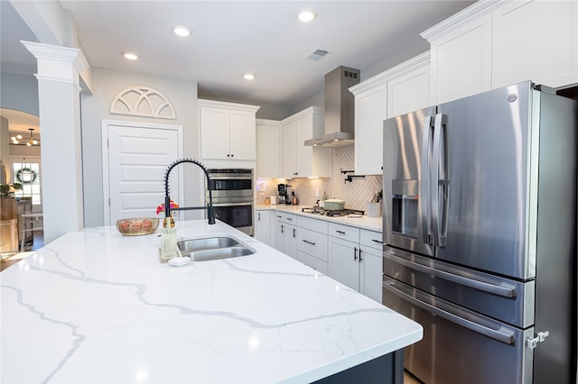 kitchen featuring appliances with stainless steel finishes, a center island with sink, white cabinetry, and wall chimney range hood