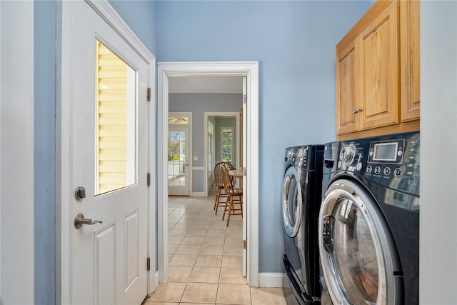 clothes washing area featuring washing machine and dryer, light tile patterned floors, and cabinets