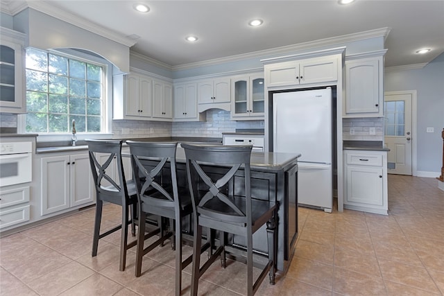 kitchen with decorative backsplash, white appliances, a center island, and white cabinetry