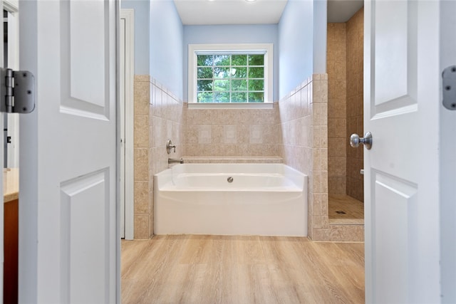 bathroom with independent shower and bath, wood-type flooring, and tile walls