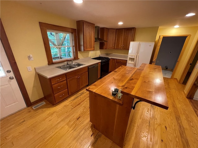 kitchen with black appliances, light hardwood / wood-style flooring, wood counters, wall chimney range hood, and sink