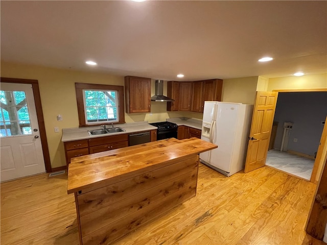 kitchen with light hardwood / wood-style floors, wood counters, sink, wall chimney exhaust hood, and black appliances