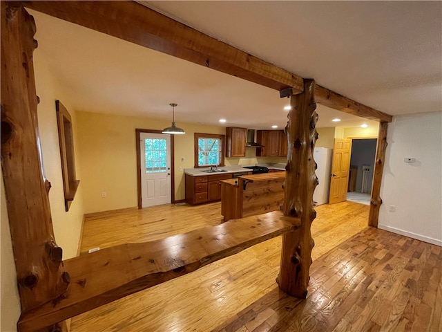 kitchen featuring hanging light fixtures, sink, kitchen peninsula, wall chimney exhaust hood, and light hardwood / wood-style floors