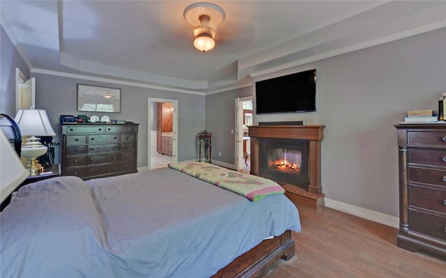 bedroom featuring light wood-type flooring, connected bathroom, a raised ceiling, crown molding, and ceiling fan